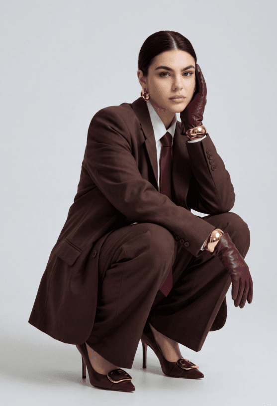 Студийный портрет женщины в коричневом костюме, бордовых перчатках и туфлях с золотыми украшениями