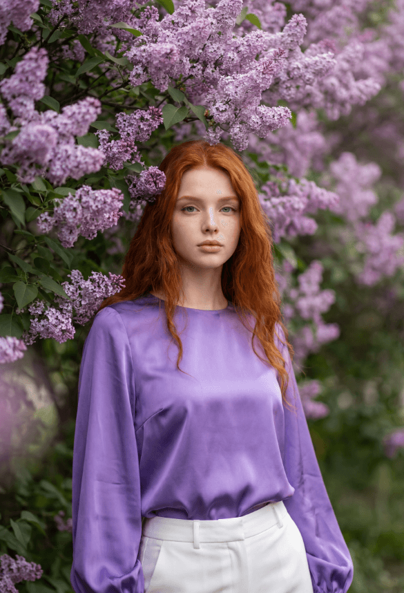 Рыжеволосая женщина в сиреневой блузке среди цветущей сирени