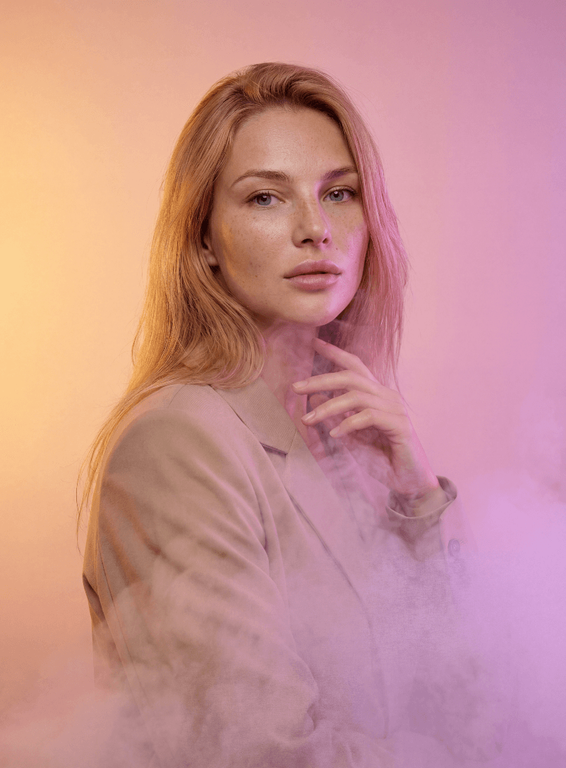 Портрет блондинки в бежевом пиджаке среди розово-оранжевого дыма