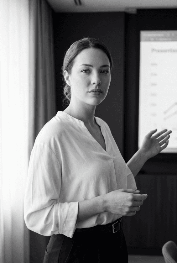 Черно-белое фото докладчицы, указывающей на проектируемый линейный график