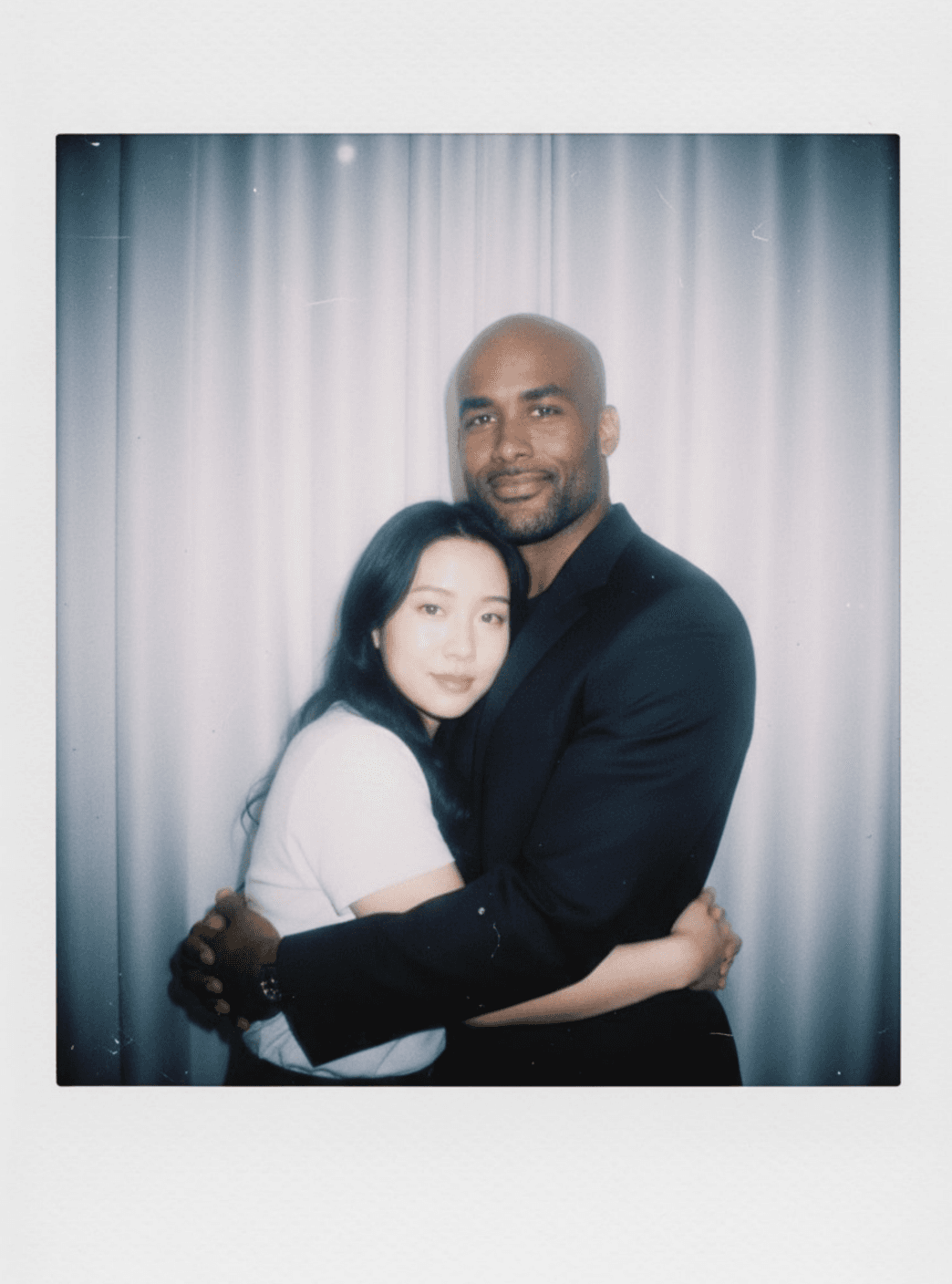 Полароид-портрет двух людей, обнимающихся на фоне белых штор