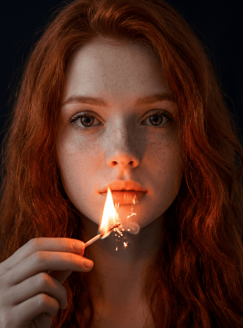 Крупный план рыжеволосой женщины с горящей бенгальской свечой у губ