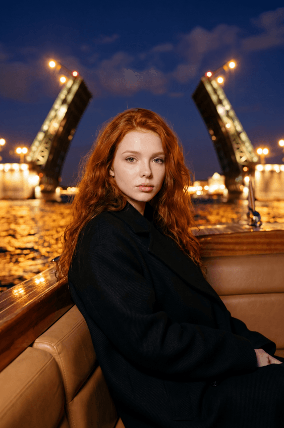 Рыжеволосая женщина на лодке у разведённого моста ночью