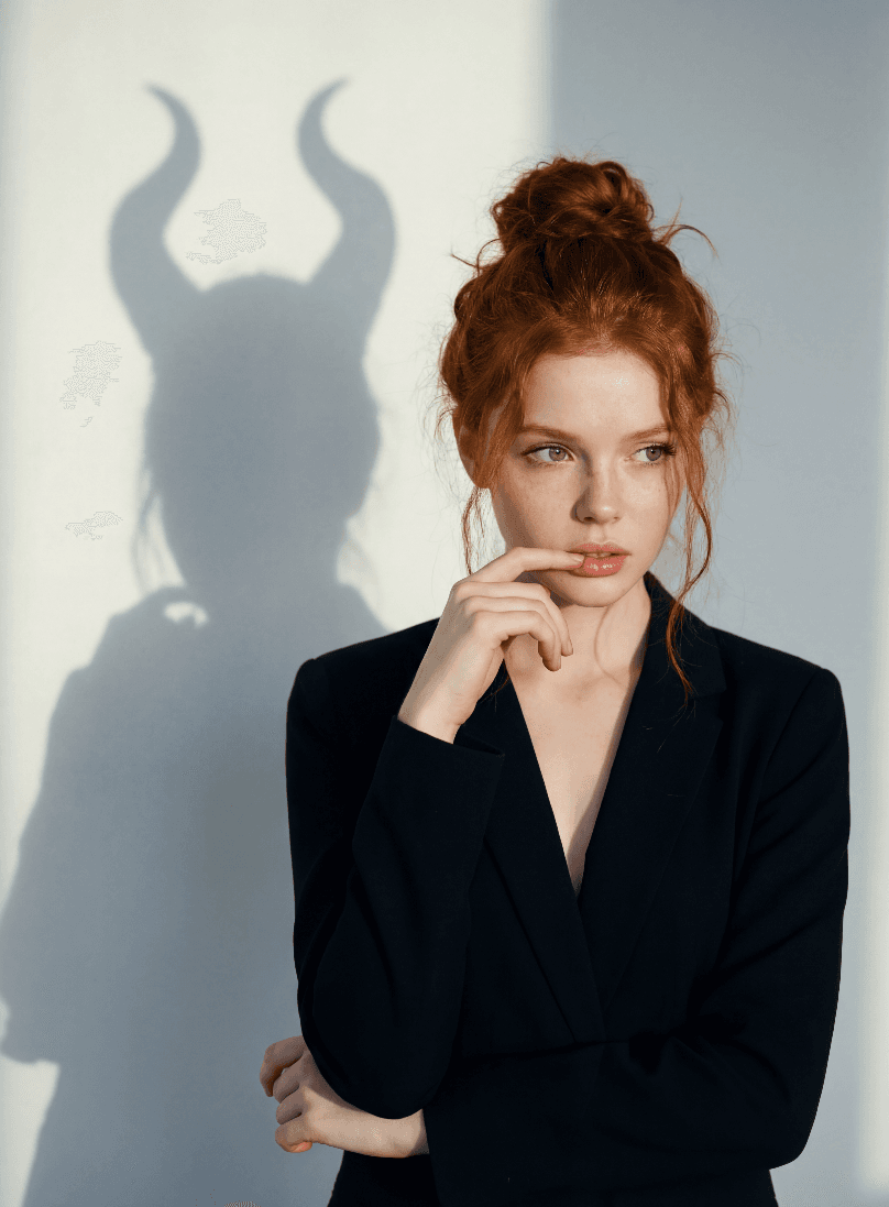 Рыжеволосая женщина в черном пиджаке, тень с рогами на стене