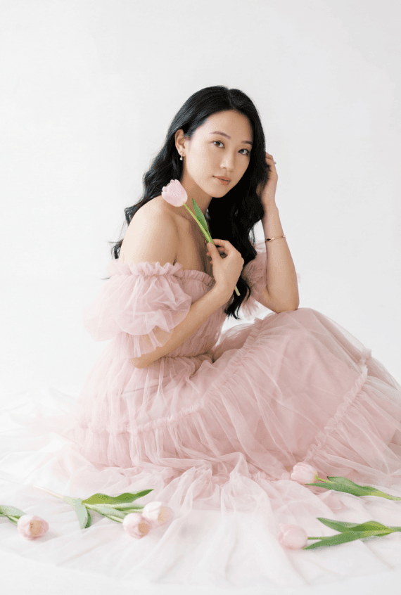 Сидящая девушка в розовом тюлевом платье с тюльпаном, белый фон