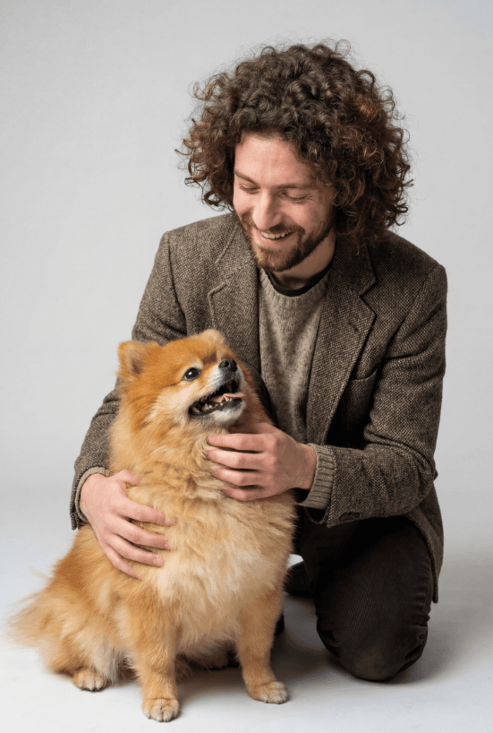 Улыбающийся мужчина гладит пушистого померанского шпица в студии