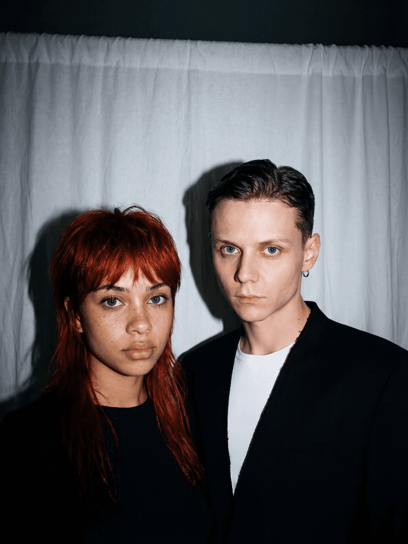 Двое молодых взрослых в студийном портрете с серьёзными лицами на фоне белой занавески