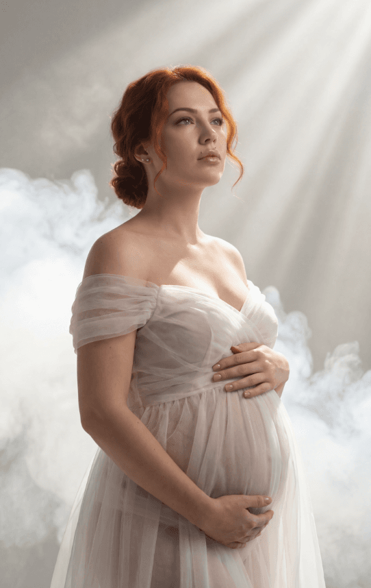 Женщина в полупрозрачном платье держит живот в мягком свете