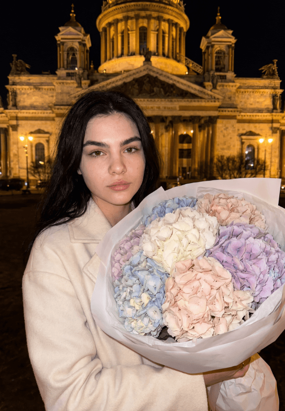 Женщина с букетом пастельных гортензий у освещённого собора ночью