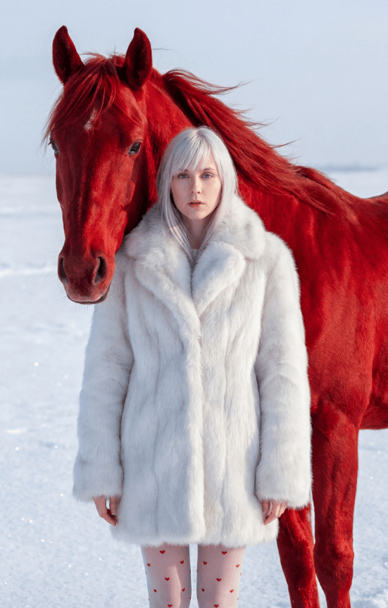 Женщина в белой шубе с красной лошадью на снегу